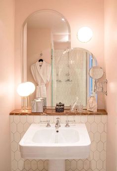 a white sink sitting under a bathroom mirror next to a bathrobe in a bathroom