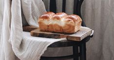 three loaves of bread sitting on top of a wooden cutting board next to a white curtain