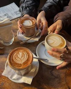 two people holding cups of coffee on top of a wooden table