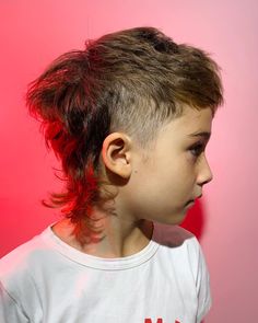 a young boy with short hair wearing a white t - shirt against a pink background