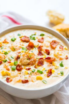 a white bowl filled with soup and topped with shrimp, corn, green onions and bacon