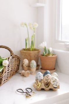 an assortment of easter eggs sitting on top of a white counter next to potted plants