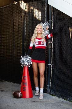 a cheerleader standing next to a red cone with silver pom - poms