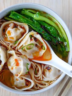 a bowl filled with noodles and vegetables on top of a wooden table next to chopsticks