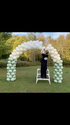 a man is standing on a ladder with balloons in the shape of clouds above him