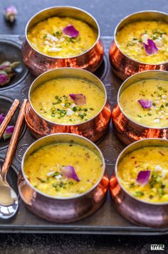 there are many bowls of soup on the tray with spoons next to each other