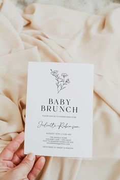 a person holding up a baby brunch card on top of a bed covered in sheets