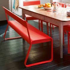 a wooden table topped with red chairs next to a bowl of fruit on top of a hard wood floor