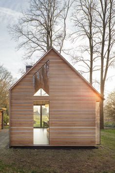 a small wooden house in the middle of a field with trees and grass around it