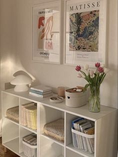 a white shelf with books and flowers on it in front of two pictures above them