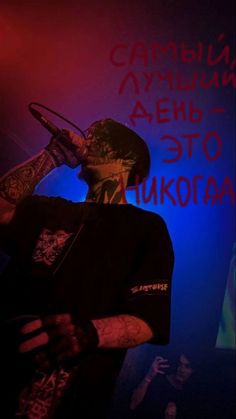 a man with tattoos on his face holding a microphone in front of a blue and red background