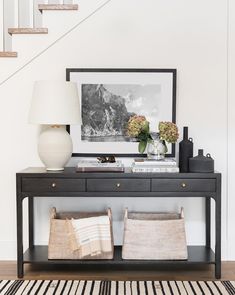 a black console table with two baskets on it and a white vase next to it