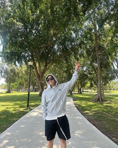 a man standing on a sidewalk with his arms in the air, wearing sunglasses and a hoodie