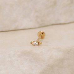 a pair of yellow gold nose rings with small diamond stones on each end, sitting on a marble surface