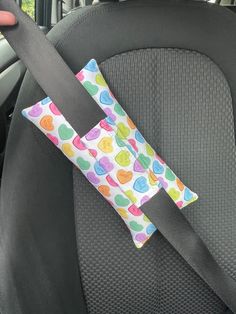 a car seat belt with a colorful polka dot design on it and a letter shaped pillow in the back