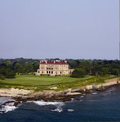 a large house sitting on top of a lush green hillside next to the ocean