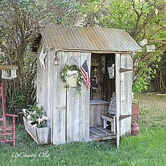 an outhouse in the middle of a yard with two chairs and a potted plant