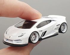 a hand holding a white toy car in it's right hand and the other hand is pointing at it