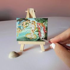 a miniature easel with a painting on it next to a seashell