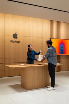 a man and woman standing in front of a desk with an apple logo on it