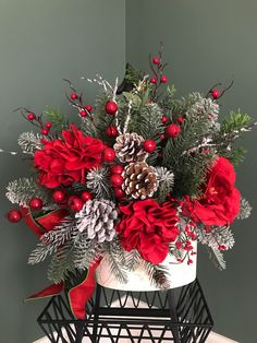 a white vase filled with red flowers and pine cones on top of a wooden table