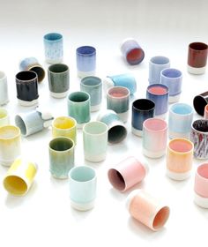 many different colored cups sitting on top of a white table together with one cup in the middle