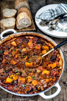 a pot filled with stew and bread on top of a wooden table