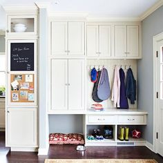 an organized mud room with white cupboards and hanging coats on the wall, along with a rug