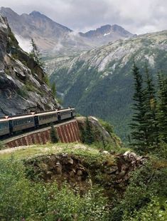 the train is traveling down the tracks in the mountains