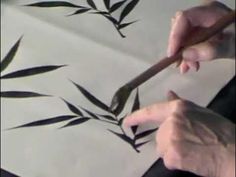 a person is using a brush to paint bamboo leaves on a sheet of white paper