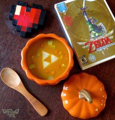 a bowl of soup next to a video game and a wooden spoon on a table