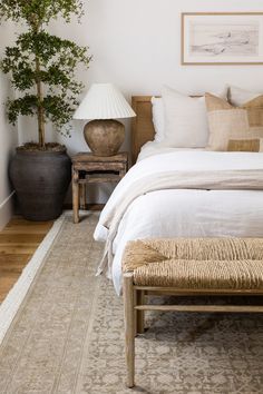 a bed with white linens and pillows on top of it next to a wooden bench