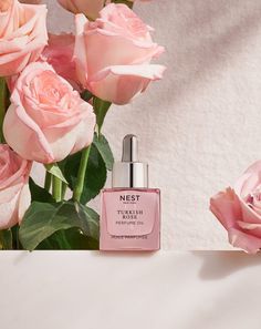 two pink roses are next to a bottle of perfume on a white surface with the words nest in it