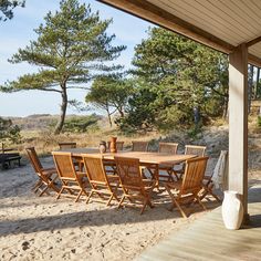 a wooden table and chairs sitting on top of a sandy beach next to pine trees