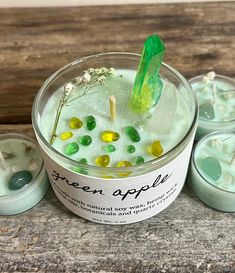 the green apple drink is in a glass with ice and candies around it on a wooden table