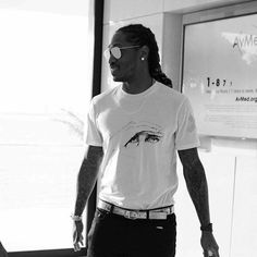 a man with dreadlocks and sunglasses is walking in an airport terminal while looking at his cell phone