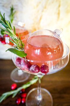 two glasses filled with drinks sitting on top of a wooden table next to cranberries