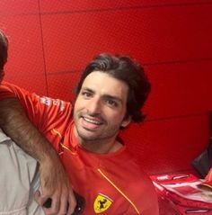 two men sitting next to each other in front of a red wall with ferrari logos on it