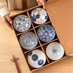 a person holding a box with six plates in it and chopsticks on the table