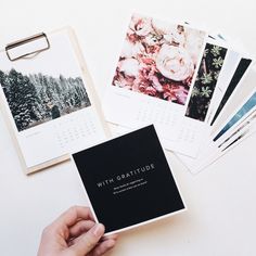 a hand holding a calendar next to several photos and magnets on a white table