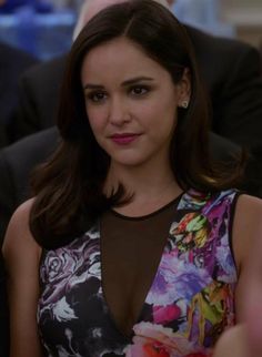 the young woman is wearing a floral dress and smiling at the camera while sitting in front of other people