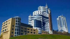 some very tall buildings on a hill in front of blue skies and green grass with trees