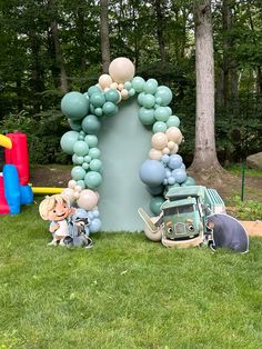 an outdoor birthday party with balloons and toys on the grass in front of a large arch