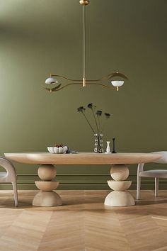 a dining room table with chairs and vases on it, in front of a green wall