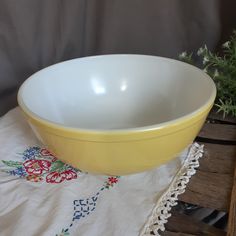 a yellow and white bowl sitting on top of a table next to a potted plant