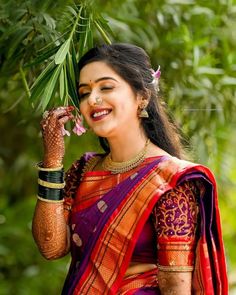 a woman in a purple and red sari holding a flower up to her face