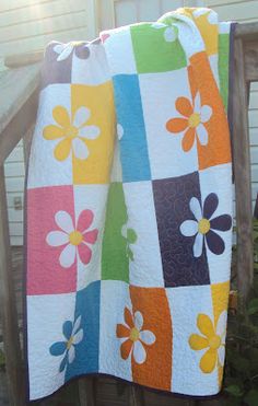 a multicolored flower quilt on a wooden porch rail next to a white house