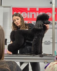 a woman holding a black poodle on top of a table