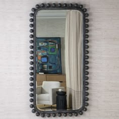 a mirror hanging on the wall above a white chair and table with a black vase