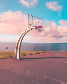 an empty basketball court next to the ocean under a blue sky with clouds in the background